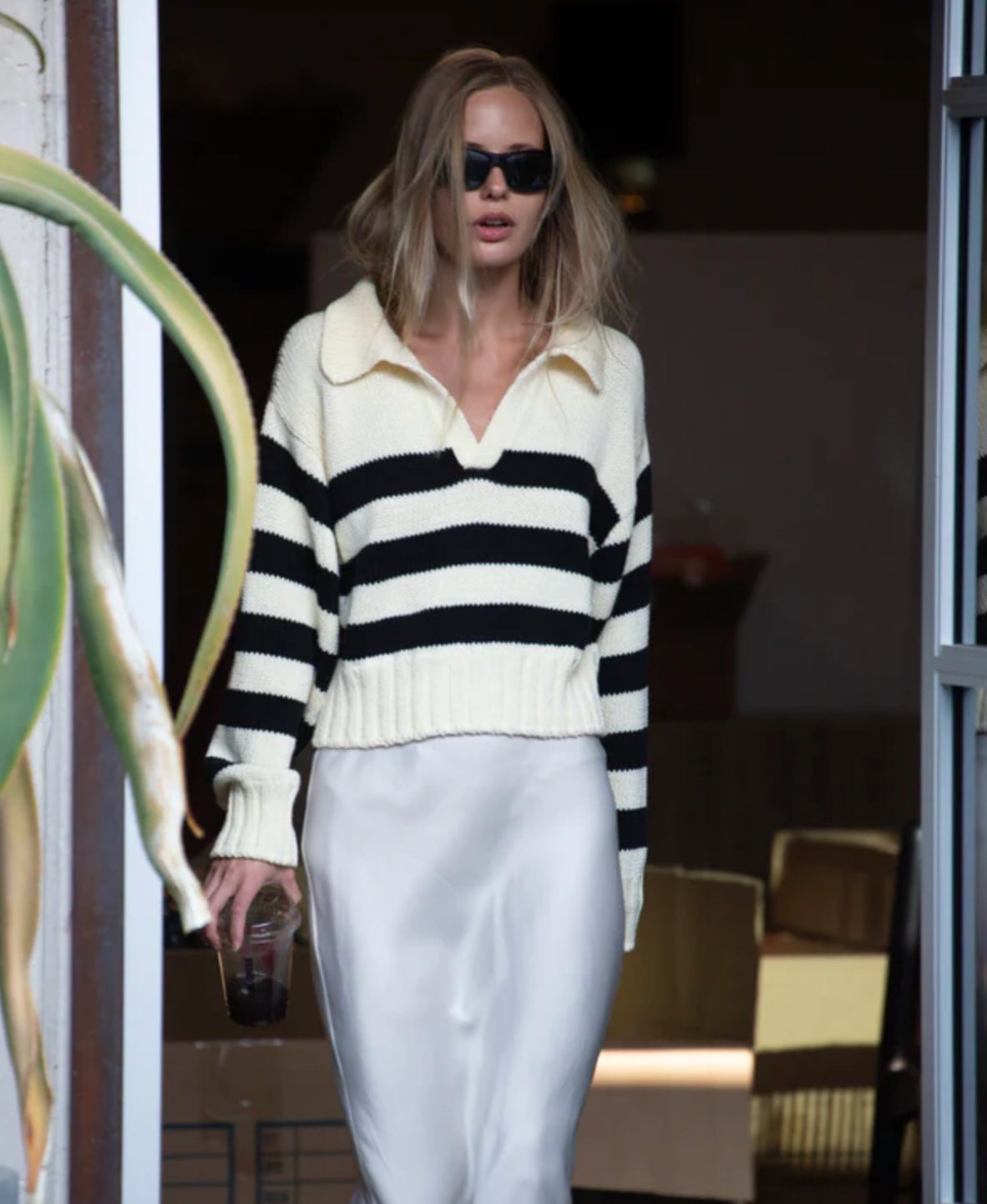 Person wearing a black and white striped sweater and white pants walking outdoors.